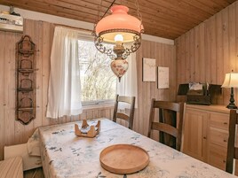 Una habitación con paneles de madera, una mesa lista para comer, una lámpara colgante y una ventana con cortinas.