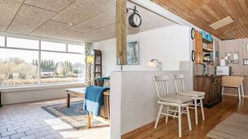 A spacious room with a large window, wooden ceiling, and a dining area with chairs and a table.