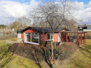 A red building with a large window, a wooden deck, and a tree in the yard. - 6 Person Holiday Home in Farso (Farso)