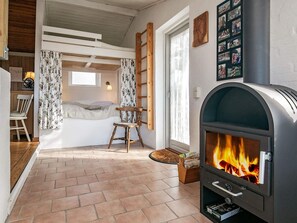 A cozy room with a bed, a wooden chair, a fireplace, and a window with curtains. - 6 Person Holiday Home in Farso (Farso)