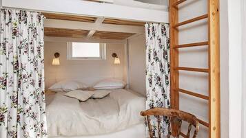 A bedroom with a bunk bed, floral curtains, a wooden ladder, and a chair.