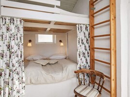 Un dormitorio con literas, cortinas florales, una escalera de madera y una silla.