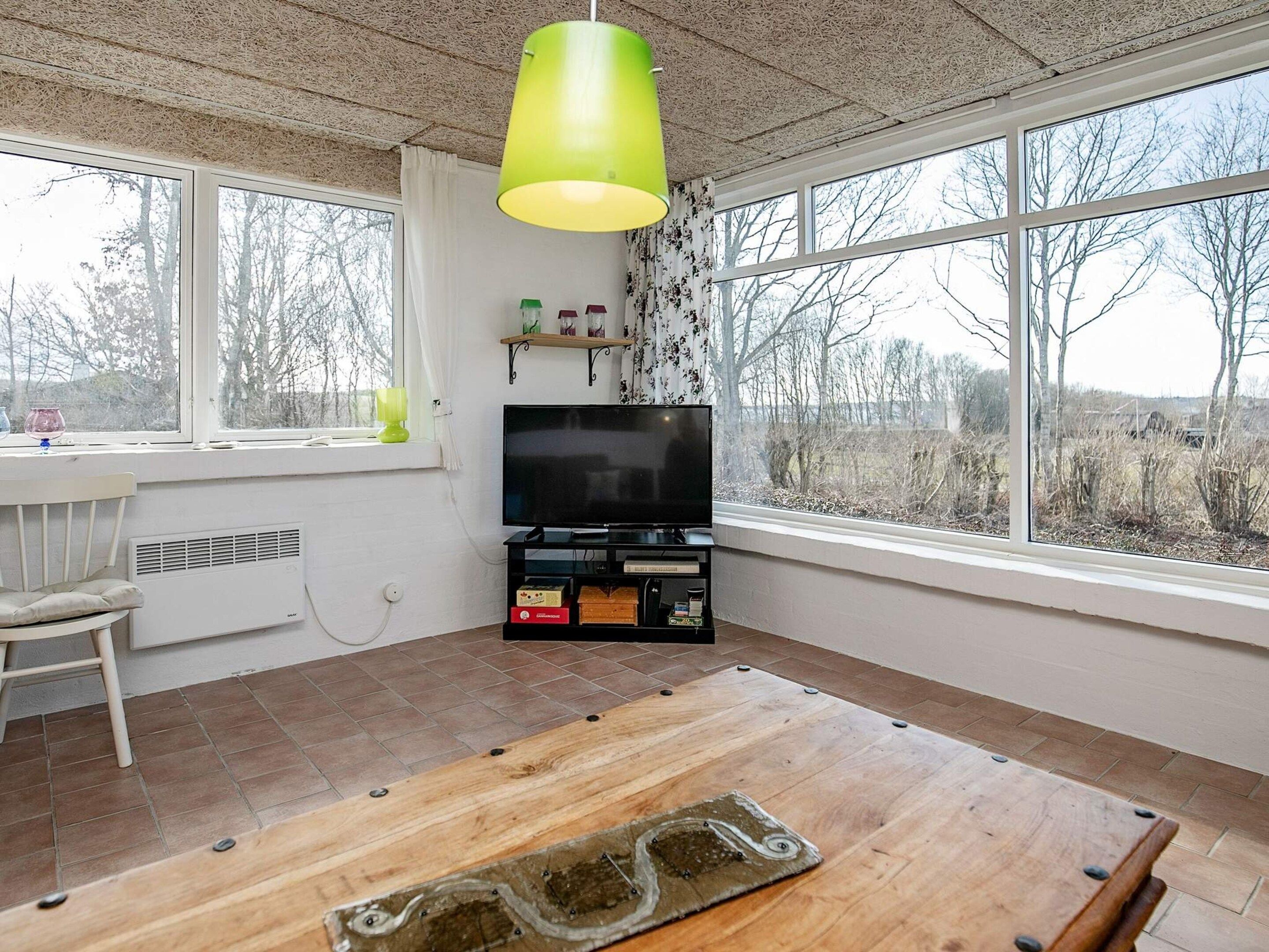 Une pièce avec une grande fenêtre, un téléviseur, une table en bois et une chaise.