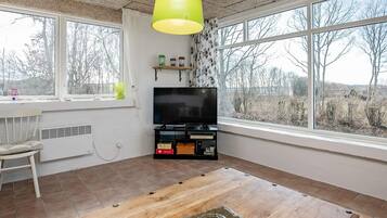 Une pièce avec une grande fenêtre, un téléviseur, une table en bois et une chaise.