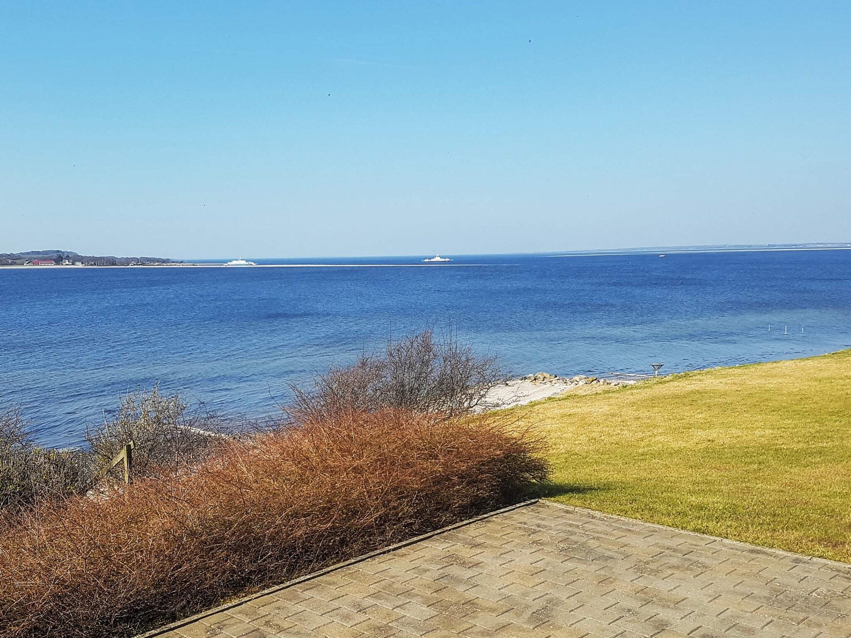 A coastal view with a paved walkway leading to a grassy area overlooking the sea.