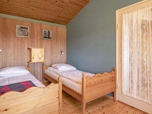 Ein Zimmer mit zwei Holzbett, einer Holzbalkendecke und einer Wand mit zwei gerahmten Bildern.