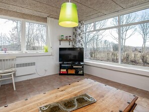 A room with a television, a wooden table, and large windows offering a view of trees. - 6 Person Holiday Home in Farso (Farso)