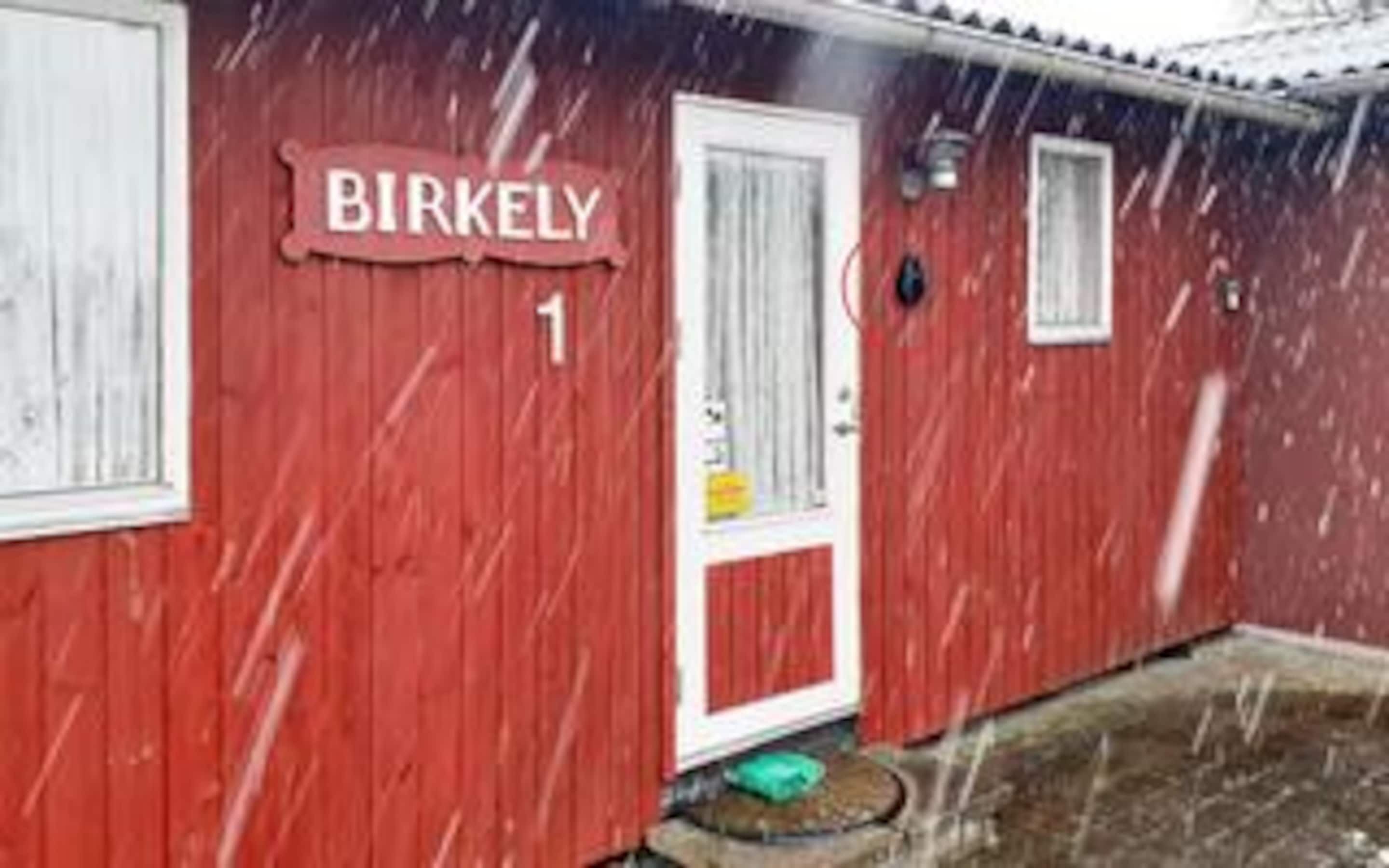 Een rood gebouw met een witte deur en een bord waarop 'BIRKELY 1' staat.
