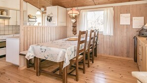 A wooden interior with a dining table set for four, a kitchen area, and a window with curtains. - 6 Person Holiday Home in Farso (Farso)