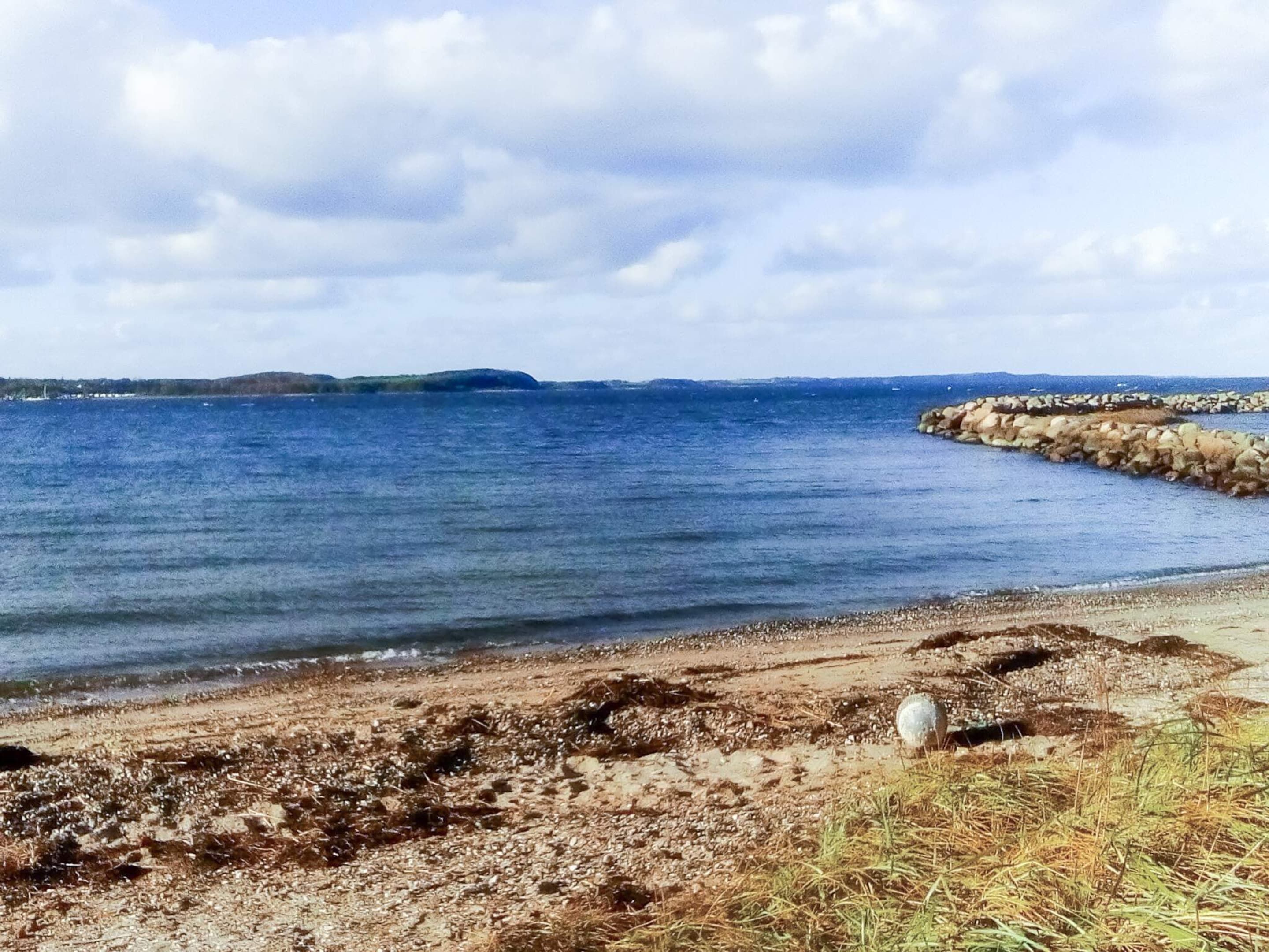 Eine Küstenlandschaft mit felsiger Uferlinie, ruhiger See und entfernten Landformen.