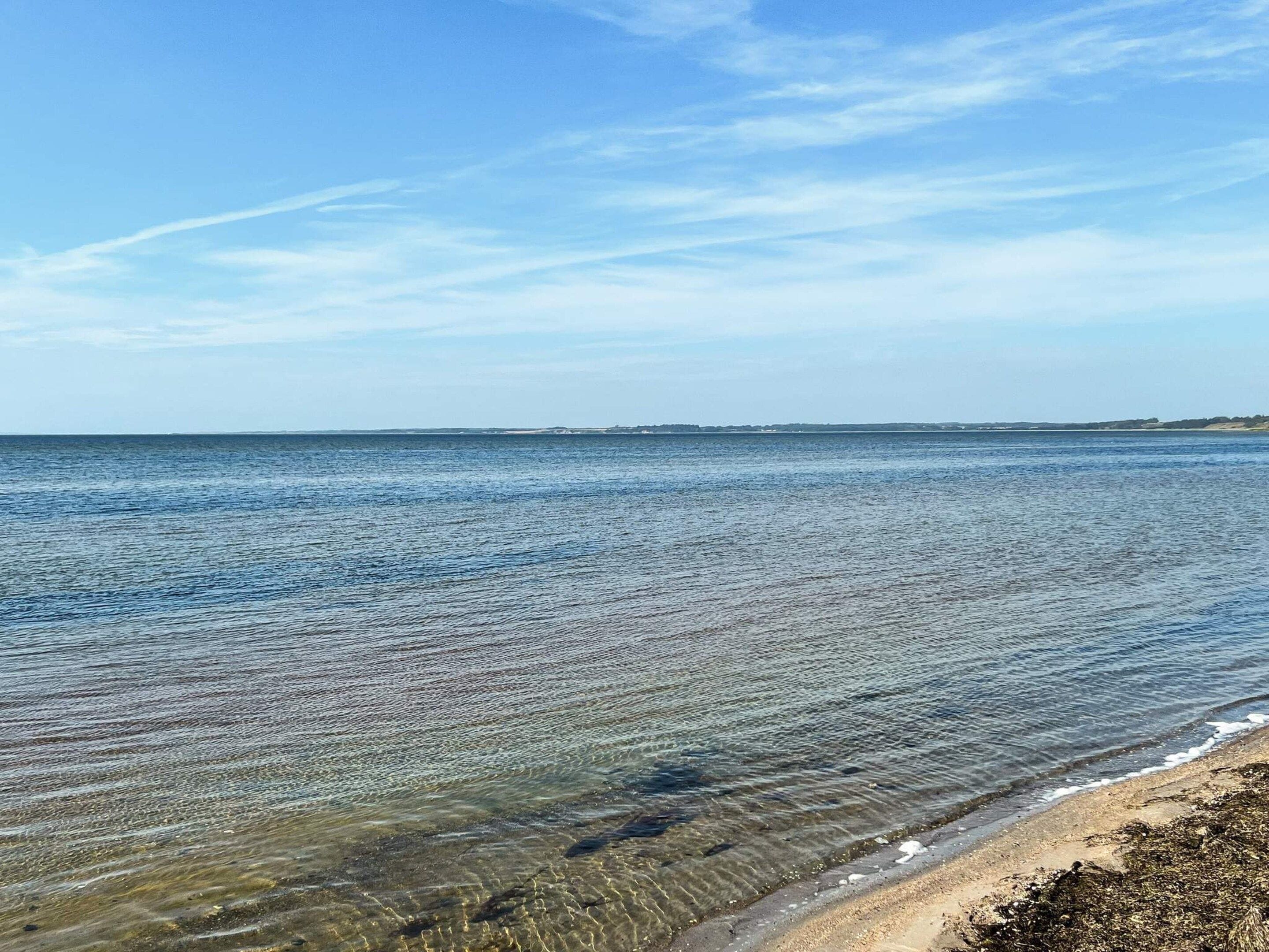 Ein klarer Blick auf einen Strand mit ruhigem Wasser und einer entfernten Küstenlinie.