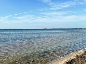 Ein klarer Blick auf einen Strand mit ruhigem Wasser und einer entfernten Küstenlinie.