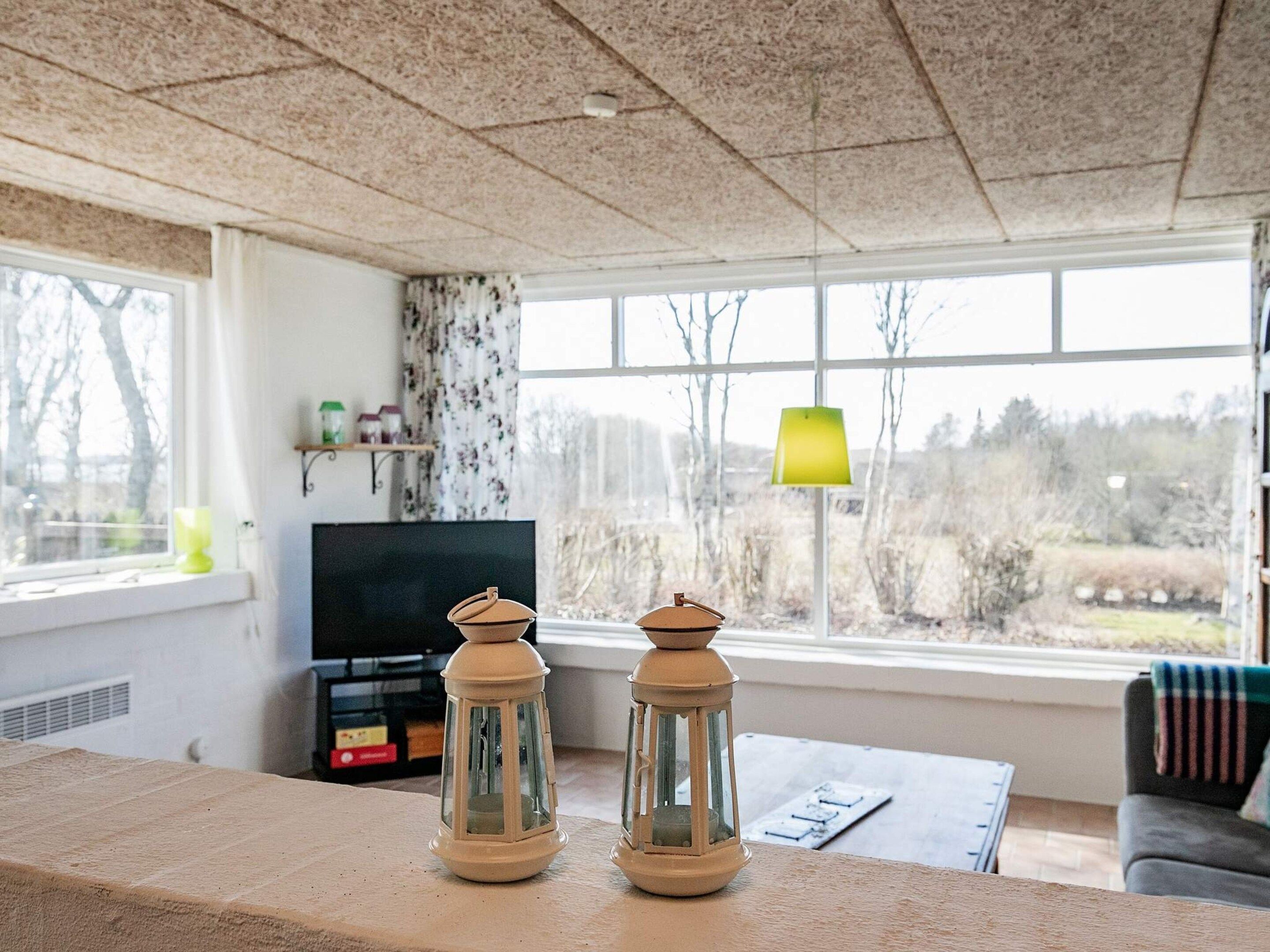 Ein Wohnzimmer mit großem Fenster, Fernseher und zwei Laternen auf einem Tisch.
