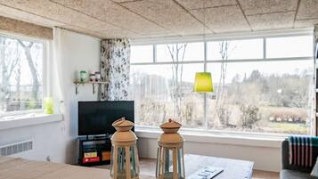 Ein Wohnzimmer mit großem Fenster, Fernseher und zwei Laternen auf einem Tisch.