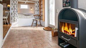 A cozy room with a bed, a wooden chair, a fireplace, and a window with curtains. - 6 Person Holiday Home in Farso (Farso)