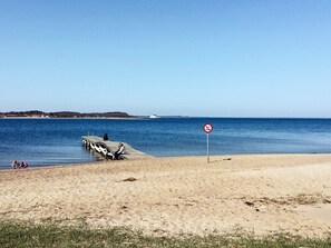 A beach with a pier, a no swimming sign, and a boat in the distance. - 6 Person Holiday Home in Farso (Farso)