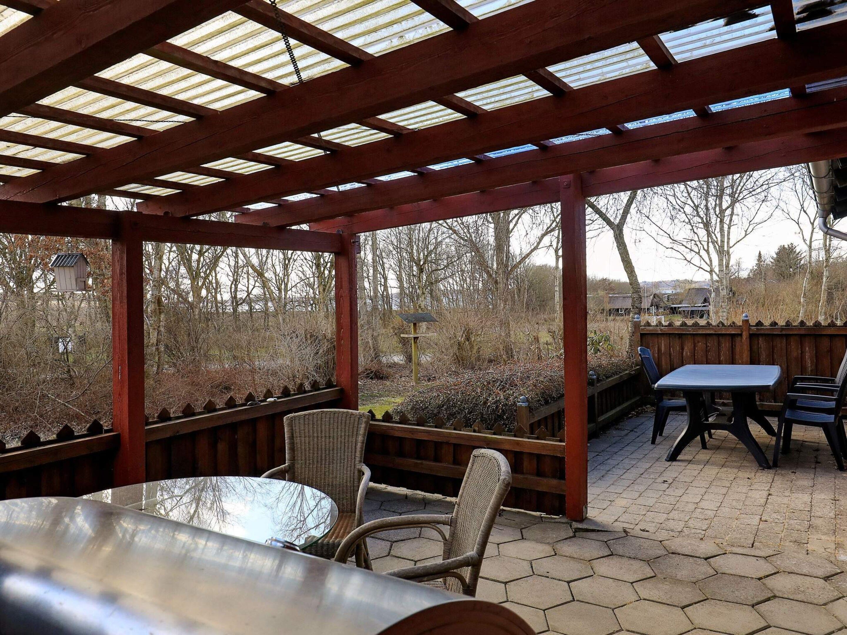 An outdoor patio with a wooden pergola, hexagonal paving, wicker chairs, and a table.