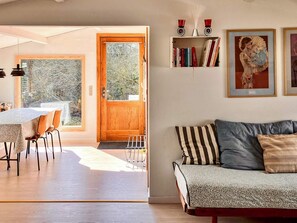 An open-plan living area with a dining table, a sofa, and a bookshelf with books and framed artwork. - 7 Person Holiday Home in Jaegerspris (Jægerspris)