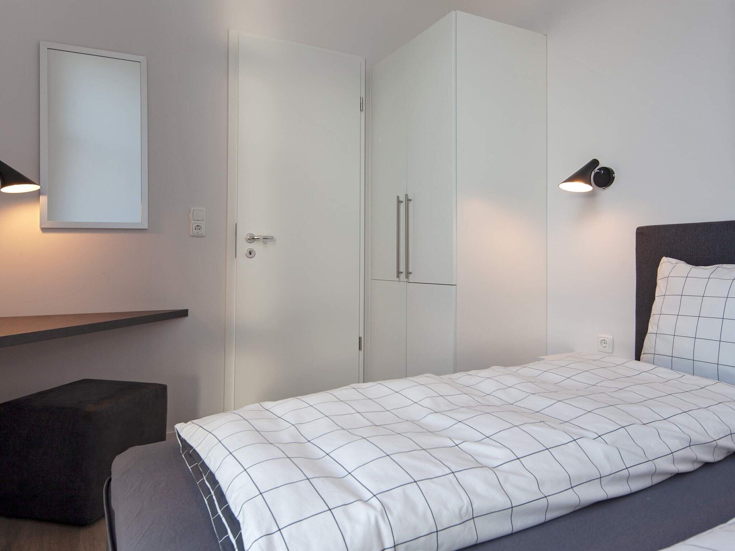 Quarto com cama, guarda-roupa, mesa de cabeceira e luminária na parede.
