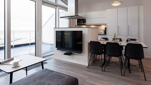 A modern kitchen with a flat-screen TV, dining area with chairs, and large windows. - 5 Star Holiday Home in Wendtorf (Wendtorf)