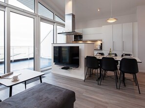 A modern kitchen with a flat-screen TV, dining area with chairs, and a balcony view. - 5 Star Holiday Home in Wendtorf (Wendtorf)