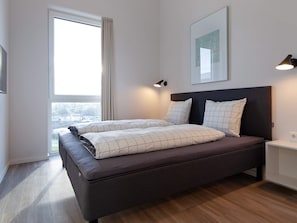 Ein modernes Schlafzimmer mit einem großen Bett, einem Nachttisch, einer Wandlampe und einem Fenster mit Vorhängen.