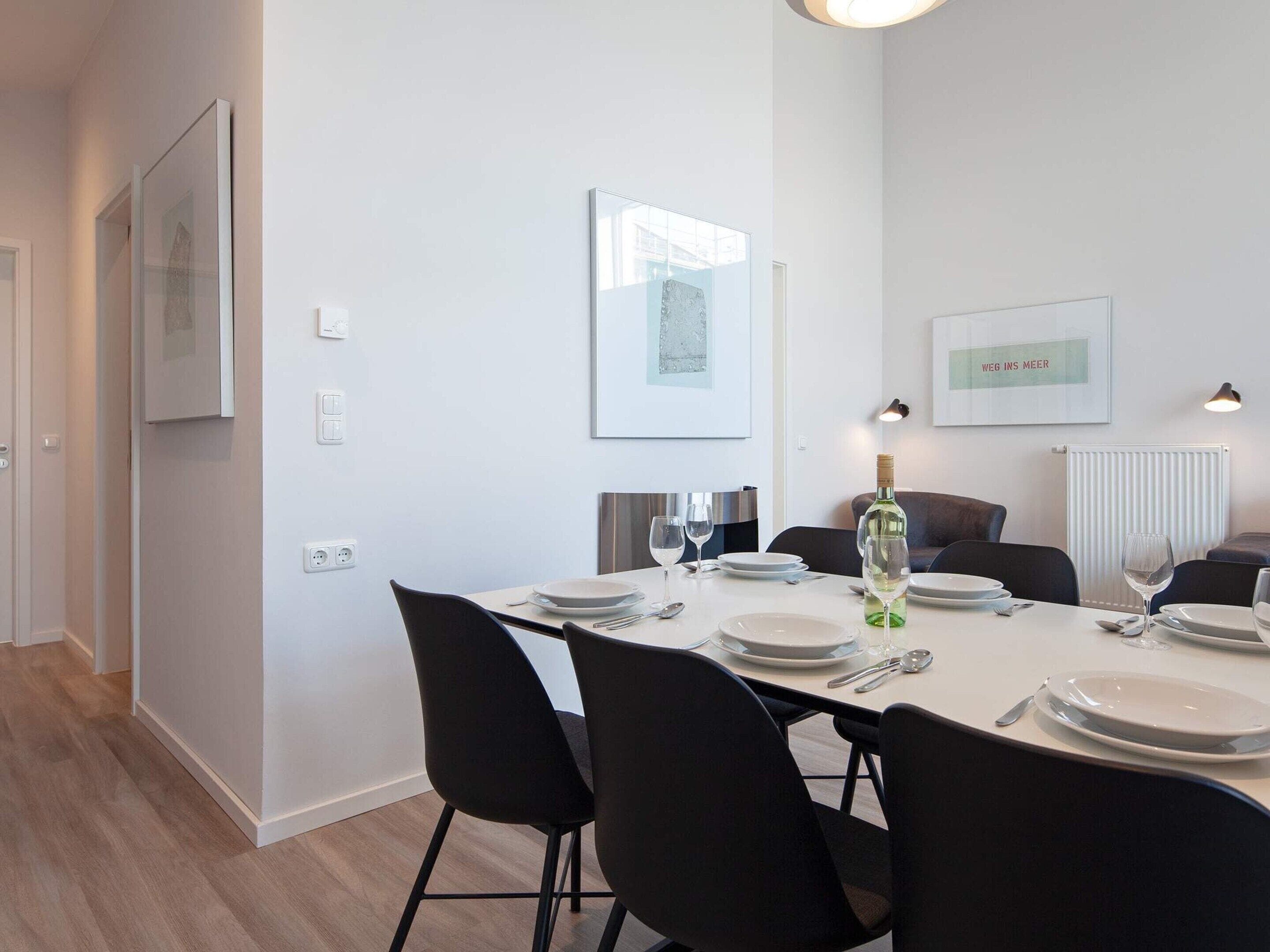 A dining area with a table set for four, chairs, a bottle of wine, and glasses.
