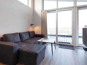 A modern living room with a sofa, a small table, and a lamp. There is a large sliding glass door leading to an outdoor balcony.