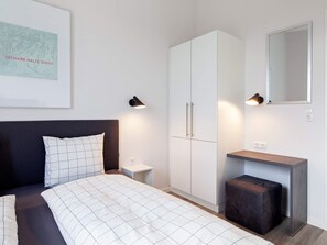 A bedroom with a bed, a wardrobe, a bedside table, a nightstand, a mirror, and a wall-mounted light fixture.