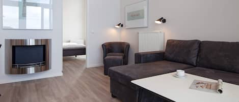 Een moderne woonkamer met een flatscreen televisie, een bank, een salontafel en een ingelijste foto aan de muur.