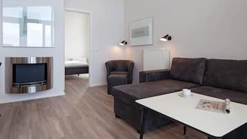Uma sala de estar moderna com televisão de tela plana, sofá, mesa de centro e um quadro na parede.
