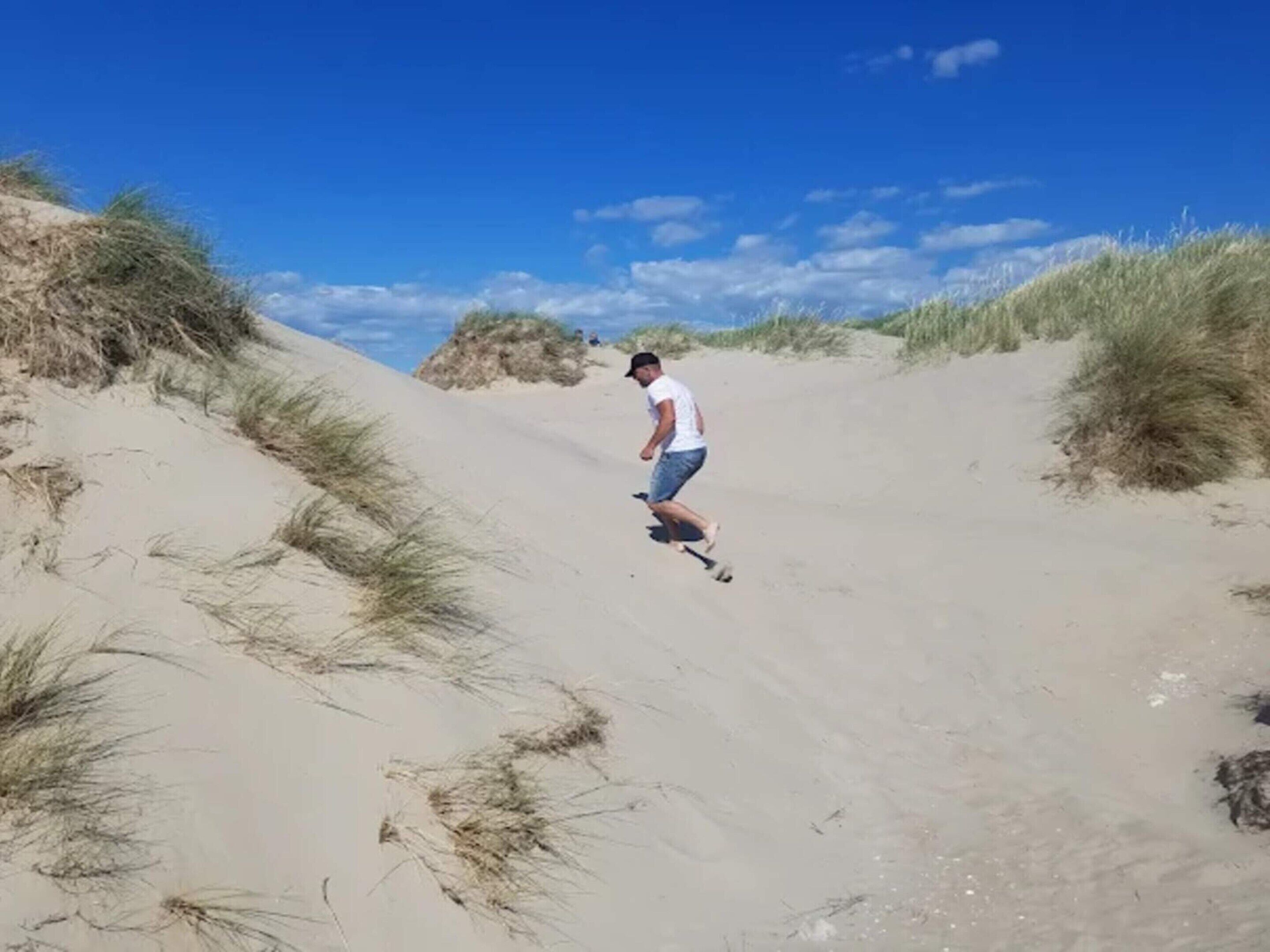 A person walking on a sandy path surrounded by dunes.