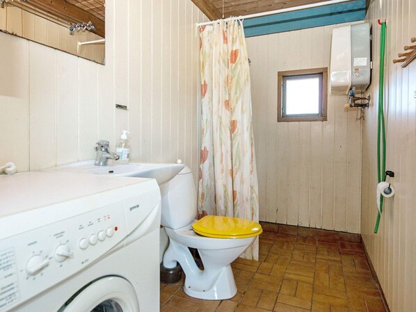A compact bathroom with a washing machine, a toilet, and a shower curtain.