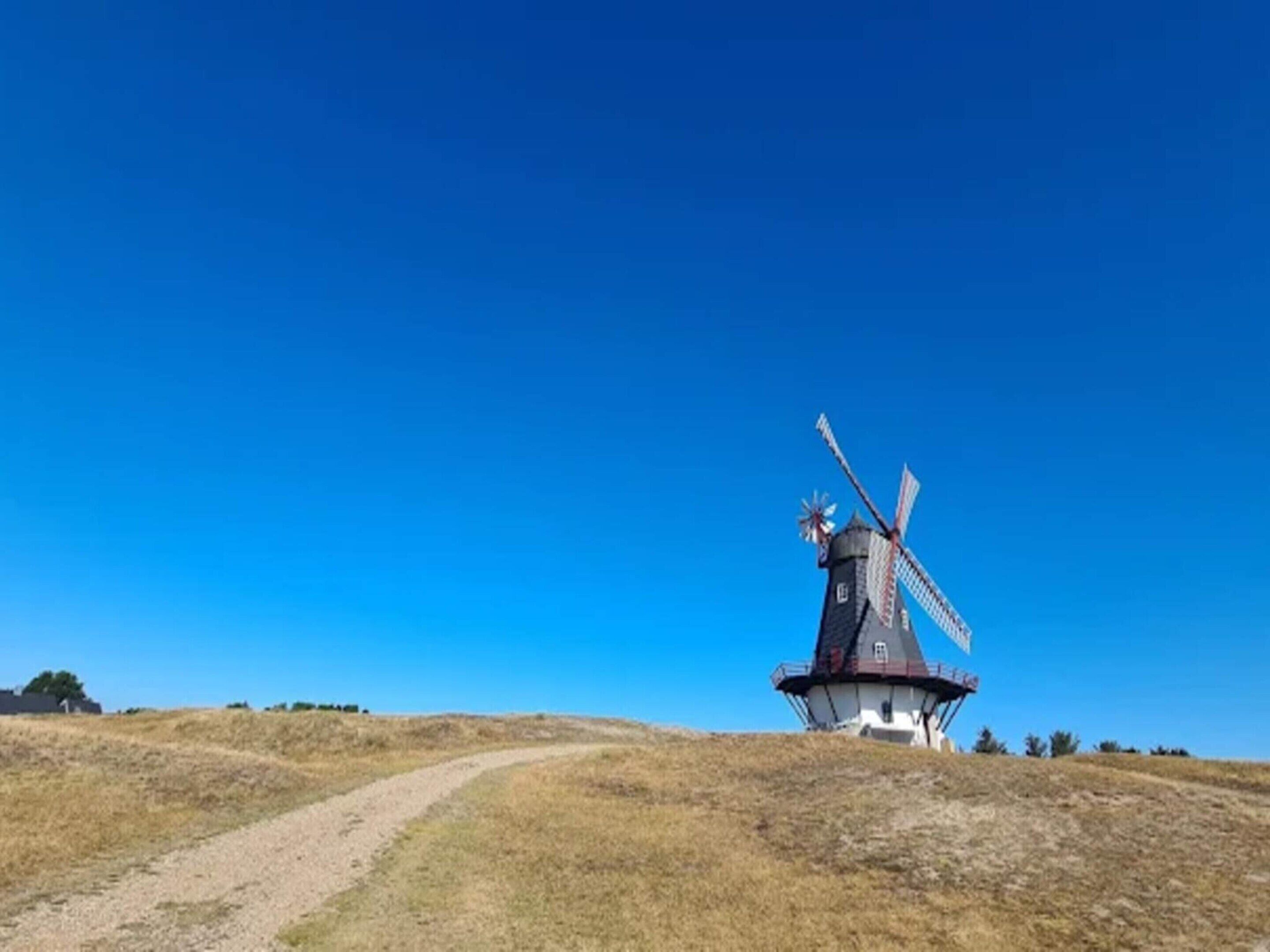 A windmill on a hill with a clear sky.
