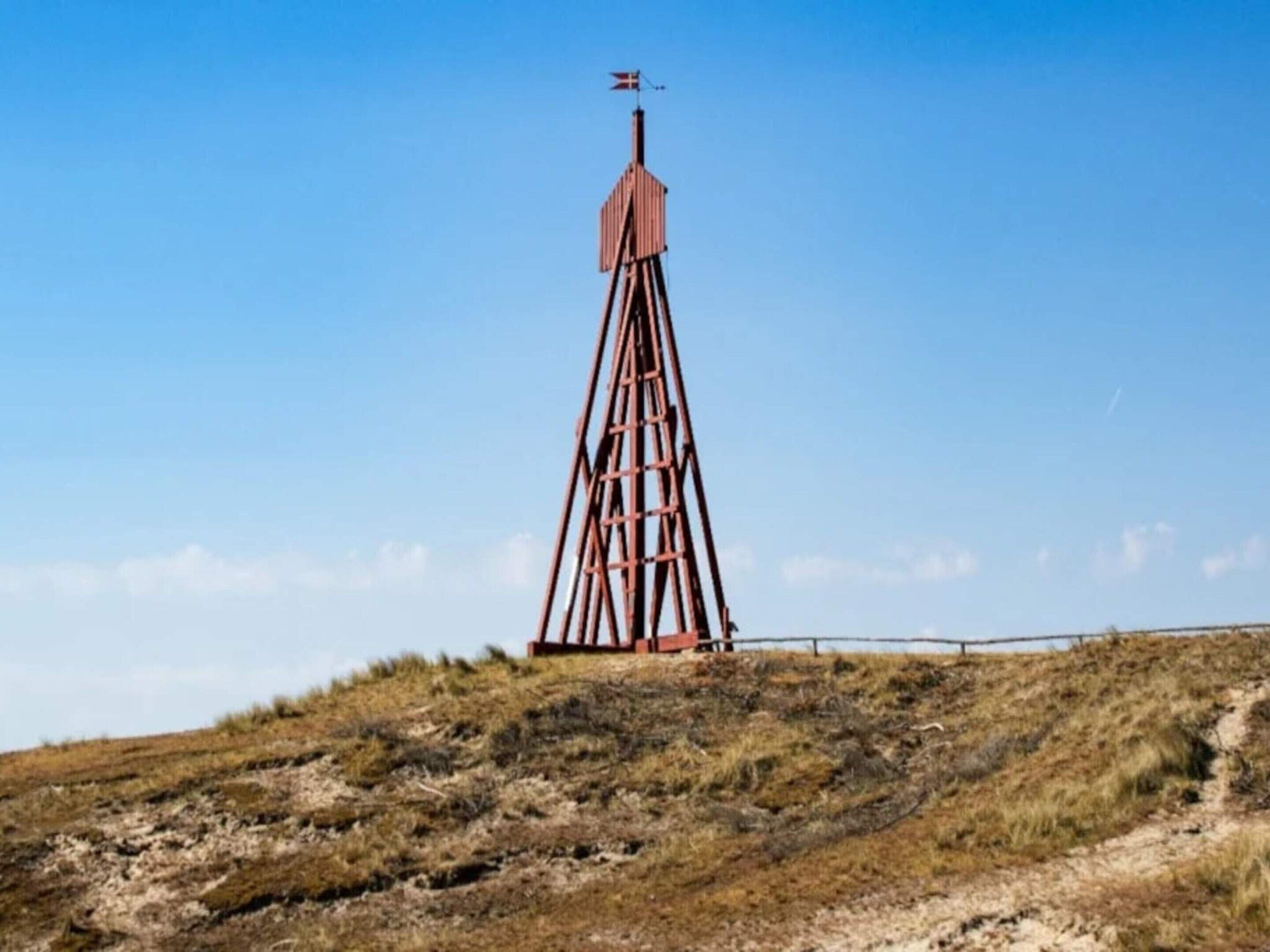 A tall, rusted metal structure with a flag on top, situated on a grassy hill with a clear sky.