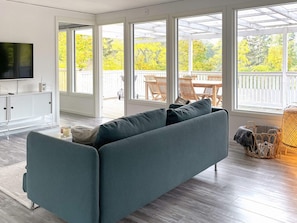 A modern living room with a sofa, a television, and a view of a wooden deck and trees.
