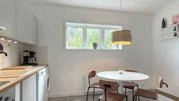 A compact kitchen with a washing machine, a coffee maker, and a dining area with a round table and chairs.