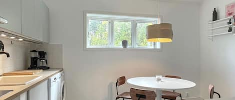 A compact kitchen with a washing machine, a coffee maker, and a dining area with a round table and chairs.