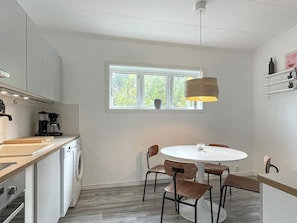 A compact kitchen with a washing machine, a coffee maker, and a dining area with a round table and chairs. - 4 Star Holiday Home in Borgholm (Borgholm)