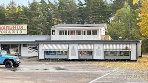 A two-story building with a sign for 'VARUHUS PORT & FRITID' and a blue vehicle parked in front. - 4 Star Holiday Home in Borgholm (Borgholm)