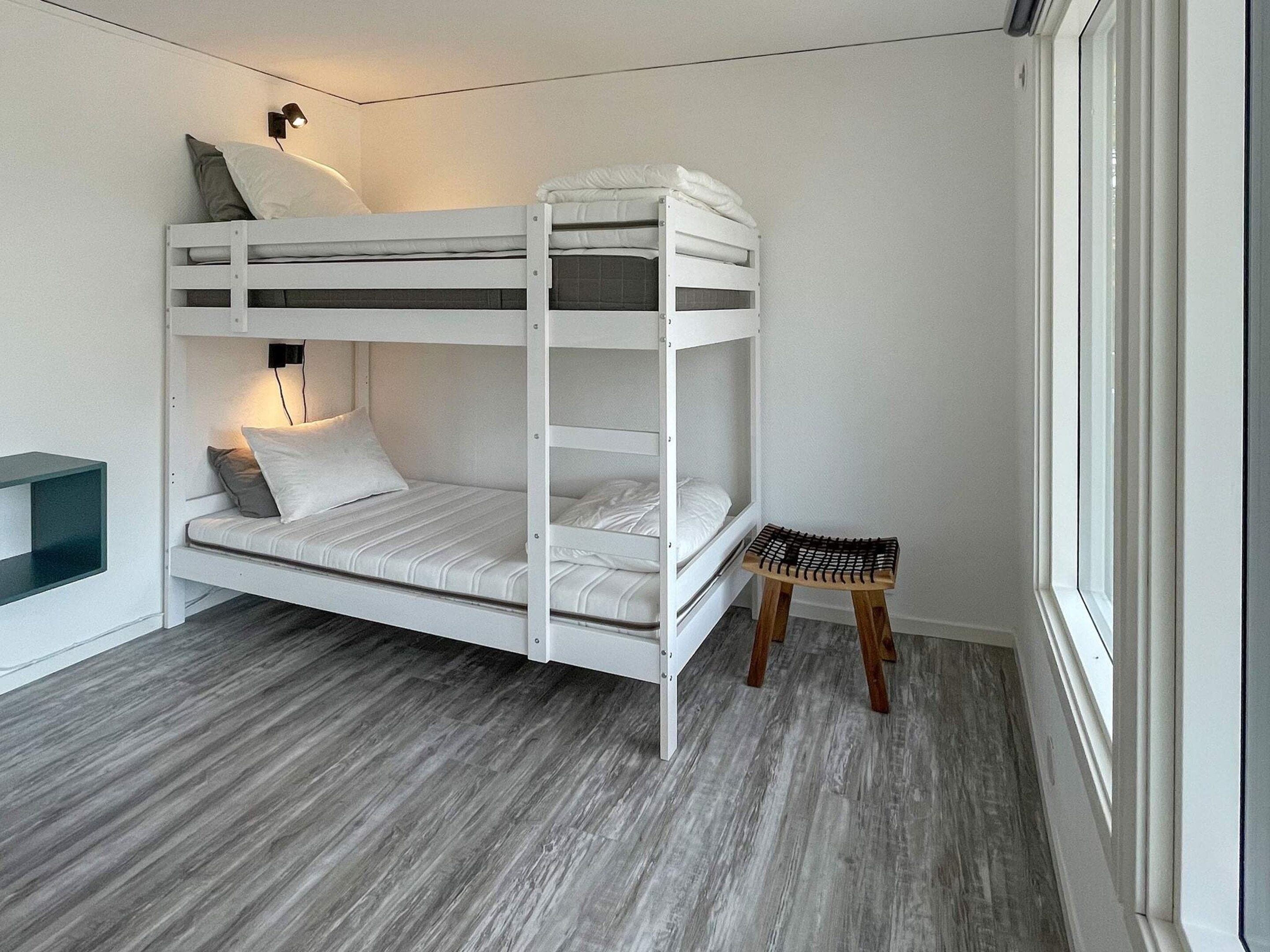 Una cama individual superpuesta con escritorio y un taburete pequeño, una lámpara de pared y una ventana.