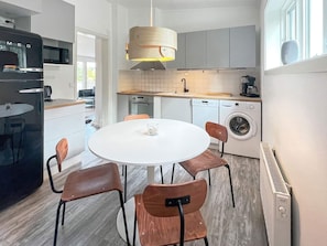 A modern kitchen with a round dining table, chairs, a hanging light fixture, and built-in appliances.