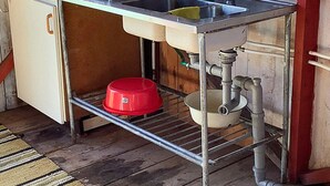 A compact kitchenette with a sink, a small refrigerator, and a metal shelf holding a red bowl and a white pot. - 4 Person Holiday Home in Lyrestad-by Traum (Lyrestad)