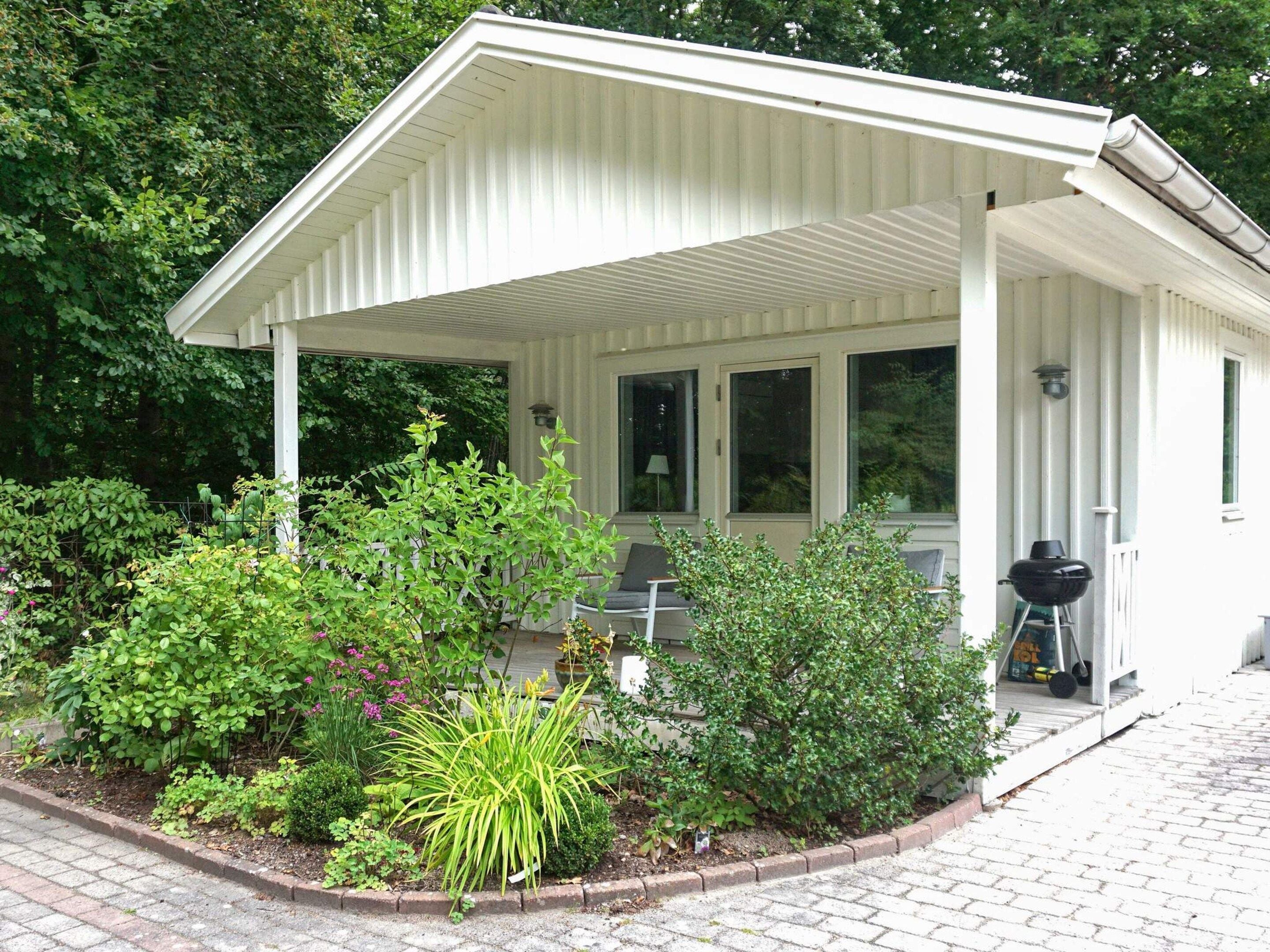 A covered porch with a brick pathway leading to it, surrounded by various plants and shrubs.
