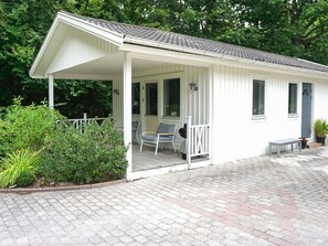 En vit byggnad med en överbyggd veranda, en bänk och en grill.