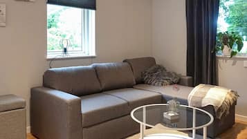 Un salón moderno con un sofá gris, una mesa de centro de vidrio y vistas a la vegetación exterior.
