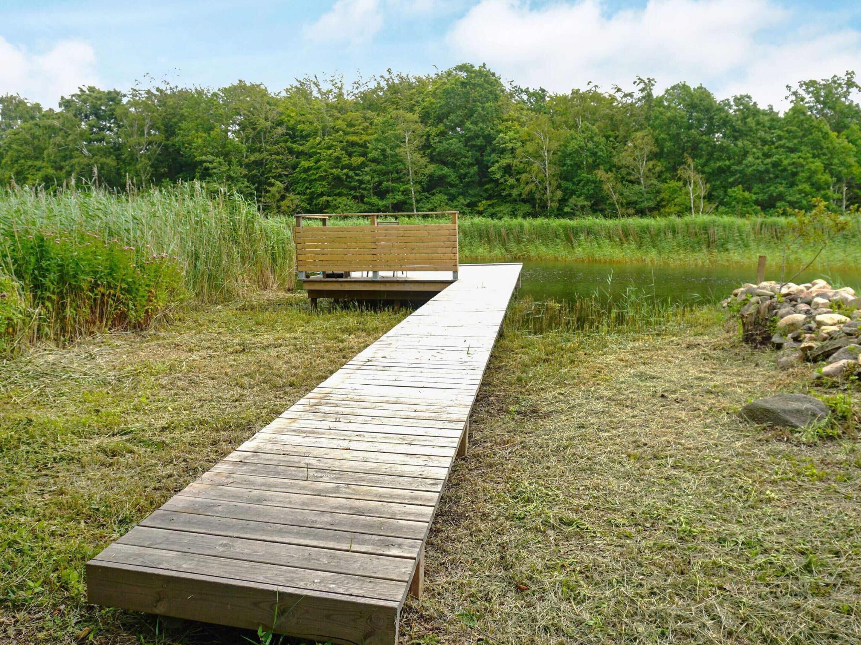 A wooden dock leading to a bench by a body of water, surrounded by grass and trees.