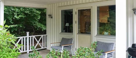 A covered porch with two chairs and a grill.