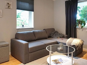 Un salón moderno con un sofá gris, una mesa de centro de vidrio y vistas a zonas verdes.