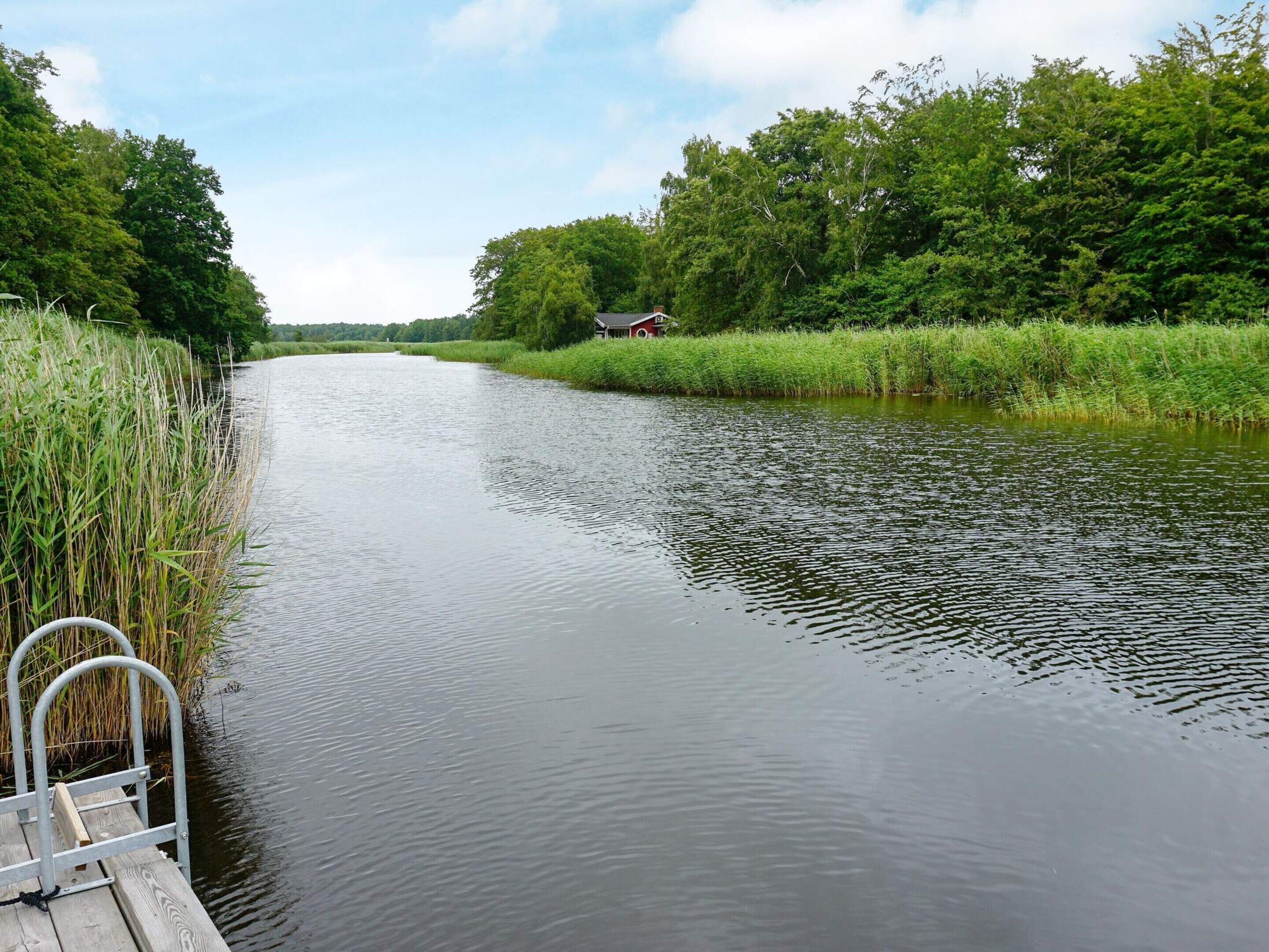 Une rivière paisible, avec une jetée en bois et un petit bâtiment sur la rive opposée.